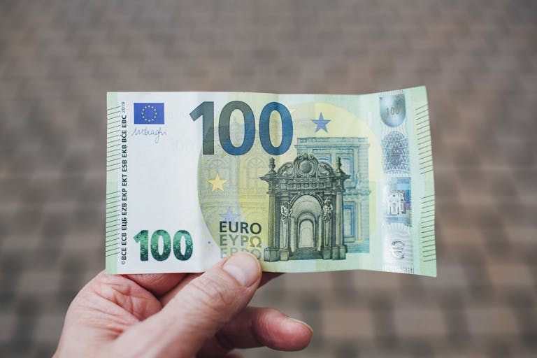 Close-up photo showing a person holding a 100 euro banknote against a blurred background.